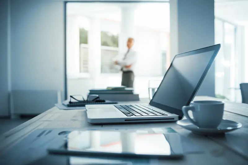 person in background with their laptop in foreground they are using for work purposes