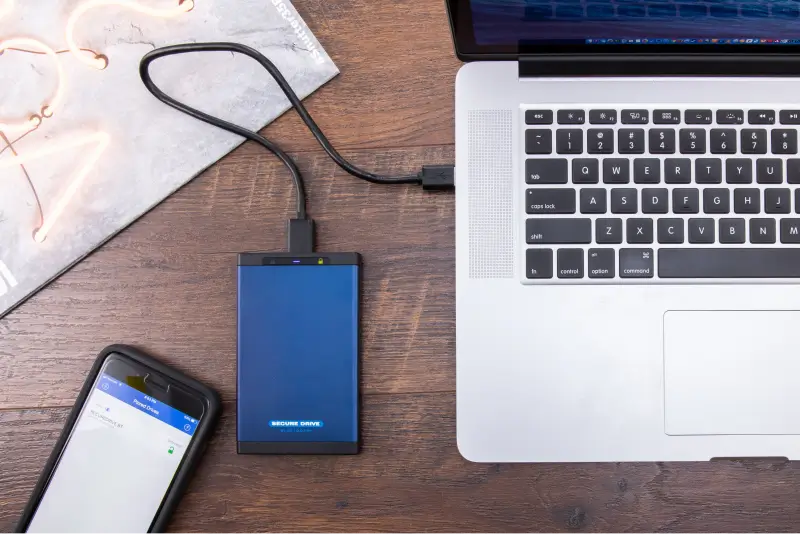 An image of SecureDrive® BT, smartphone, and laptop on a desk.