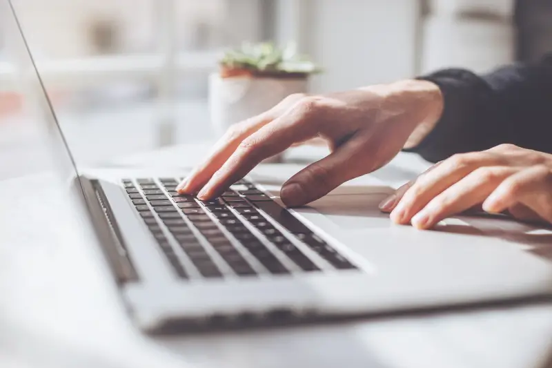 An image of a person with their hand on a MacBook’s keyboard.